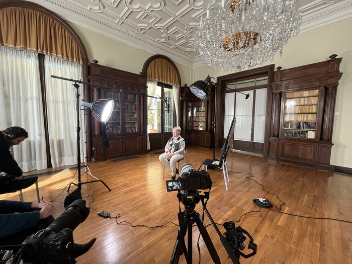 Filming an interview in a classic room with a chandelier and bookshelves