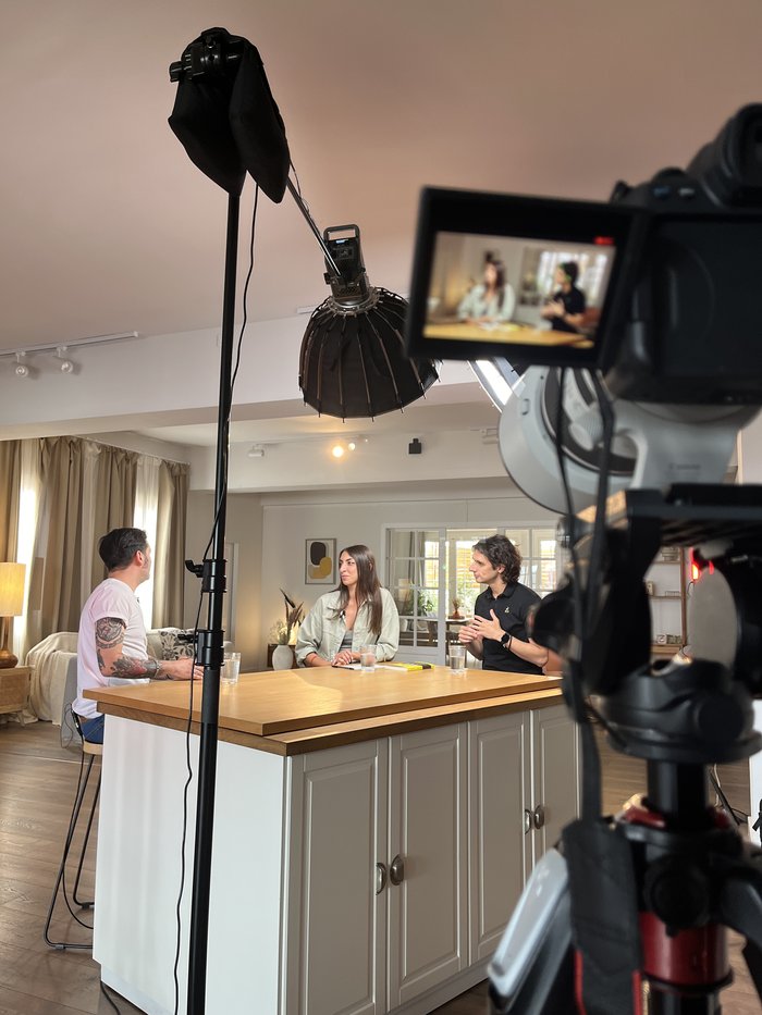 Camera monitor showing a podcast-style interview in a bright kitchen