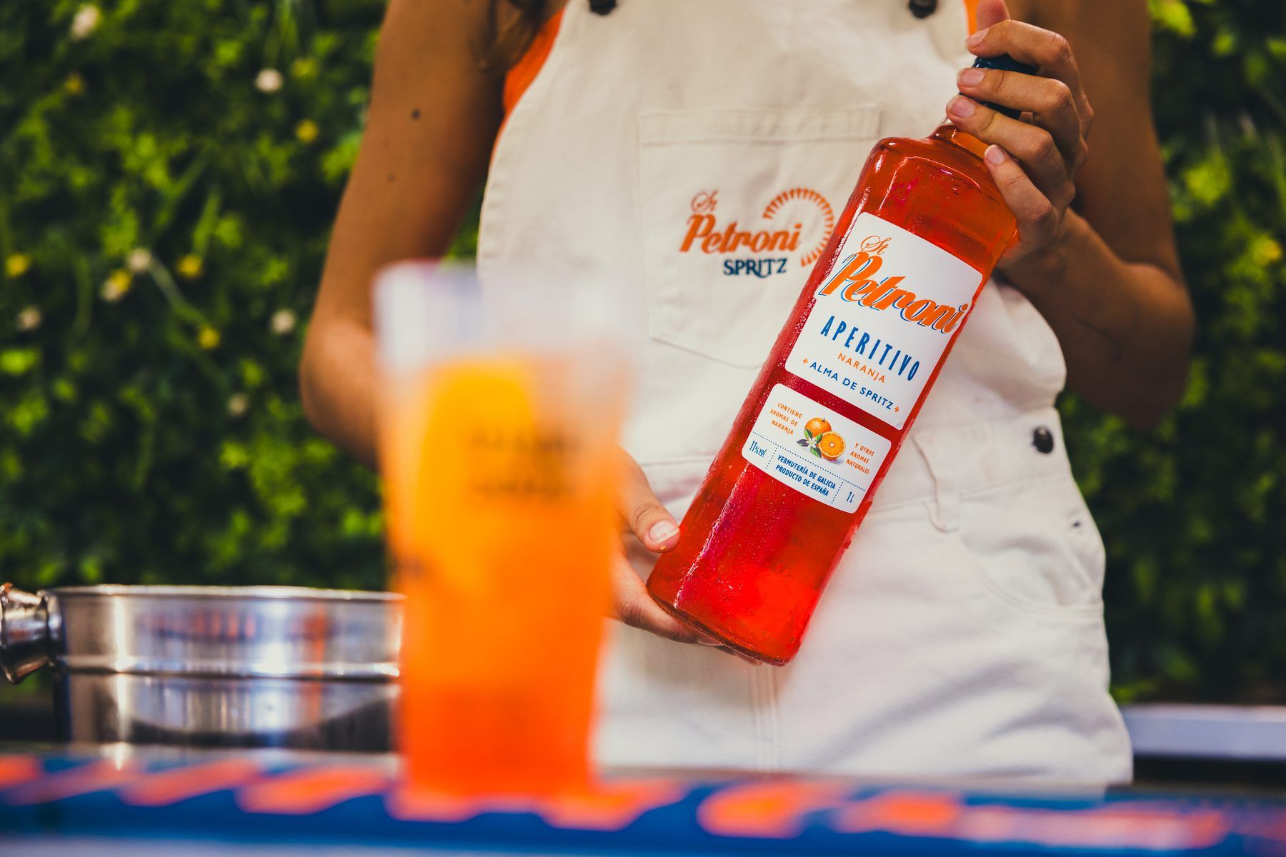Hand holding a bottle of St Petroni Aperitivo with an orange cocktail glass in the foreground